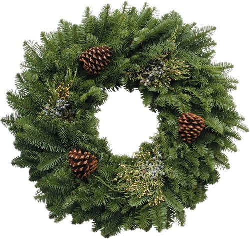 A circular green wreath made of pine branches, decorated with several brown pinecones and sprigs of greenery, set against a white background.