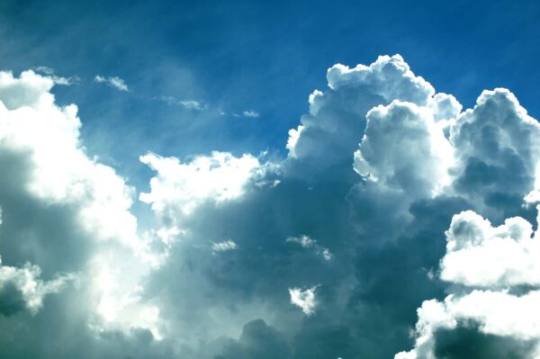 Bright white cumulus clouds against a vibrant blue sky, with sunlight streaming through, creating dramatic light and shadow contrasts.
