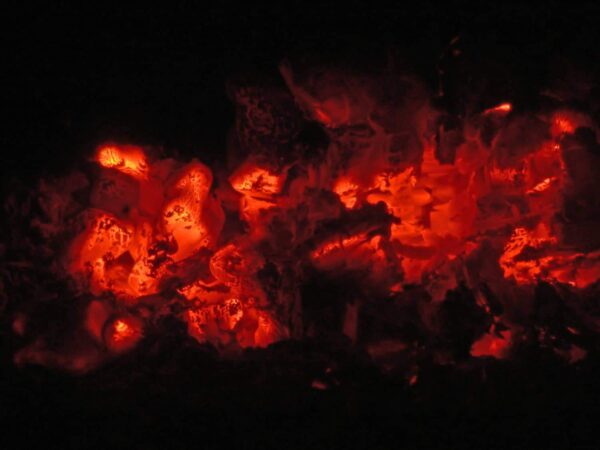 Glowing red and orange embers are surrounded by darkness, showing the heat and light produced by the burning remains of wood or charcoal.