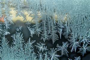 Close-up of intricate ice crystals forming frosty patterns on a window, with light shining softly through the glass, highlighting the delicate shapes and textures of the frozen designs.