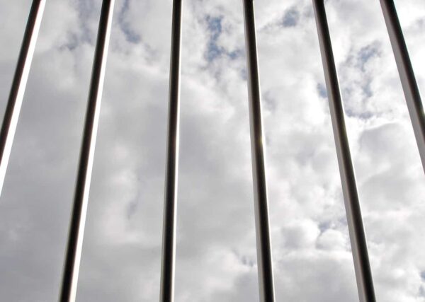 Vertical metal bars in the foreground with a cloudy sky visible in the background. The image suggests a view as if looking through a barrier or fence.