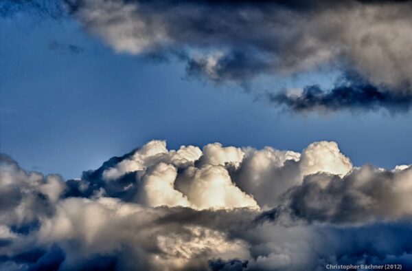Billowing white and gray clouds fill the sky under patches of blue, illuminated dramatically by sunlight.