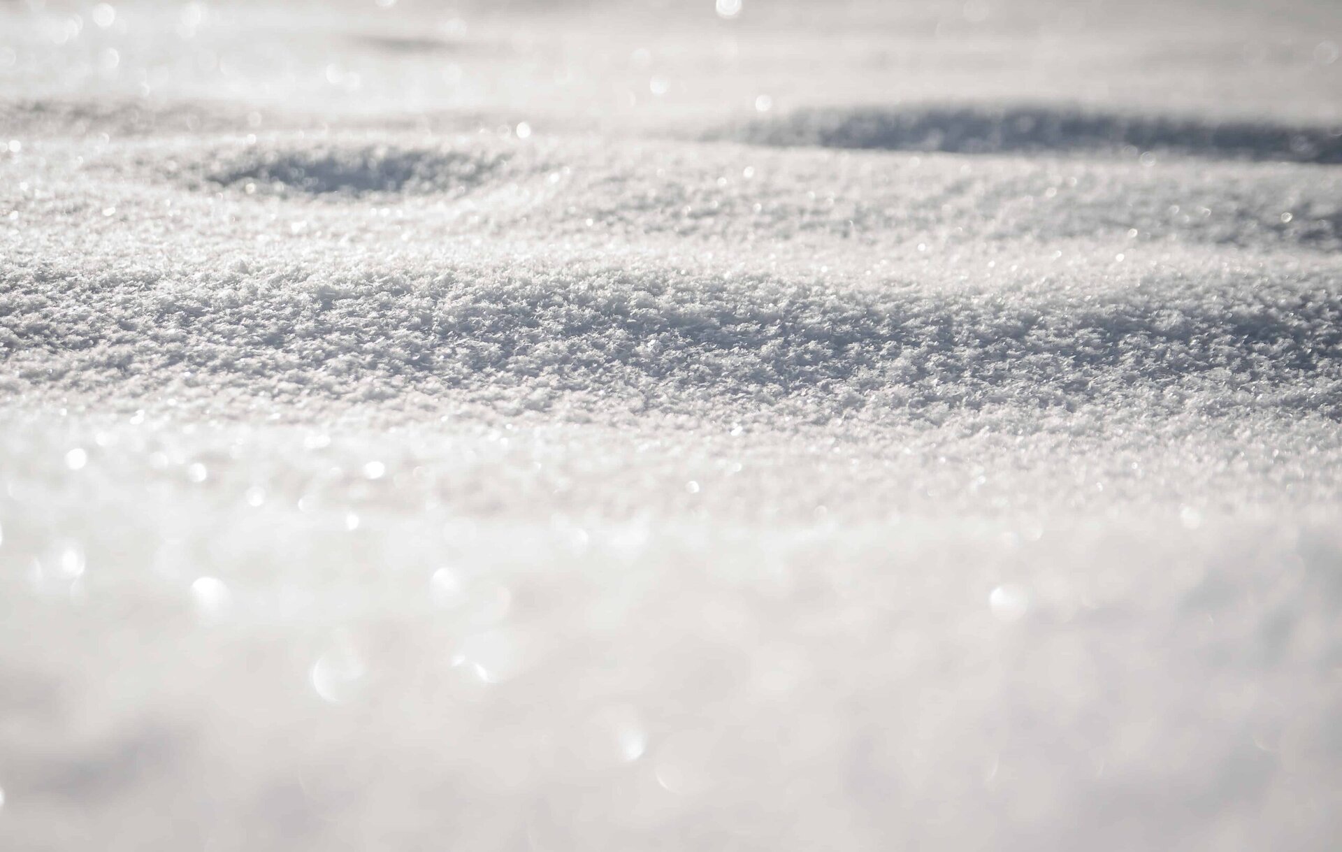 Close-up of a snow-covered surface with soft shadows and sparkling ice crystals, creating a textured, wintry landscape under bright sunlight.