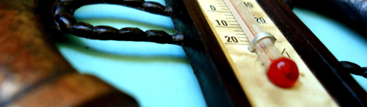 Close-up of a thermometer with a red liquid indicator, showing a temperature below 20 degrees, placed on a blue surface with some dark objects partially visible in the background.