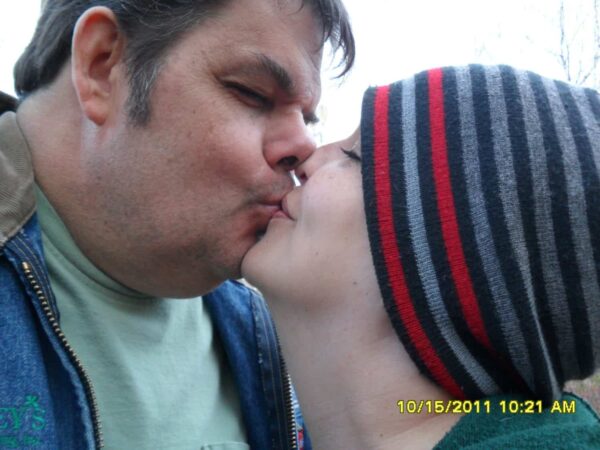 A man and a person wearing a striped beanie are kissing outdoors. The photo is close-up, and the timestamp at the bottom shows 10/15/2011 10:21 AM..
