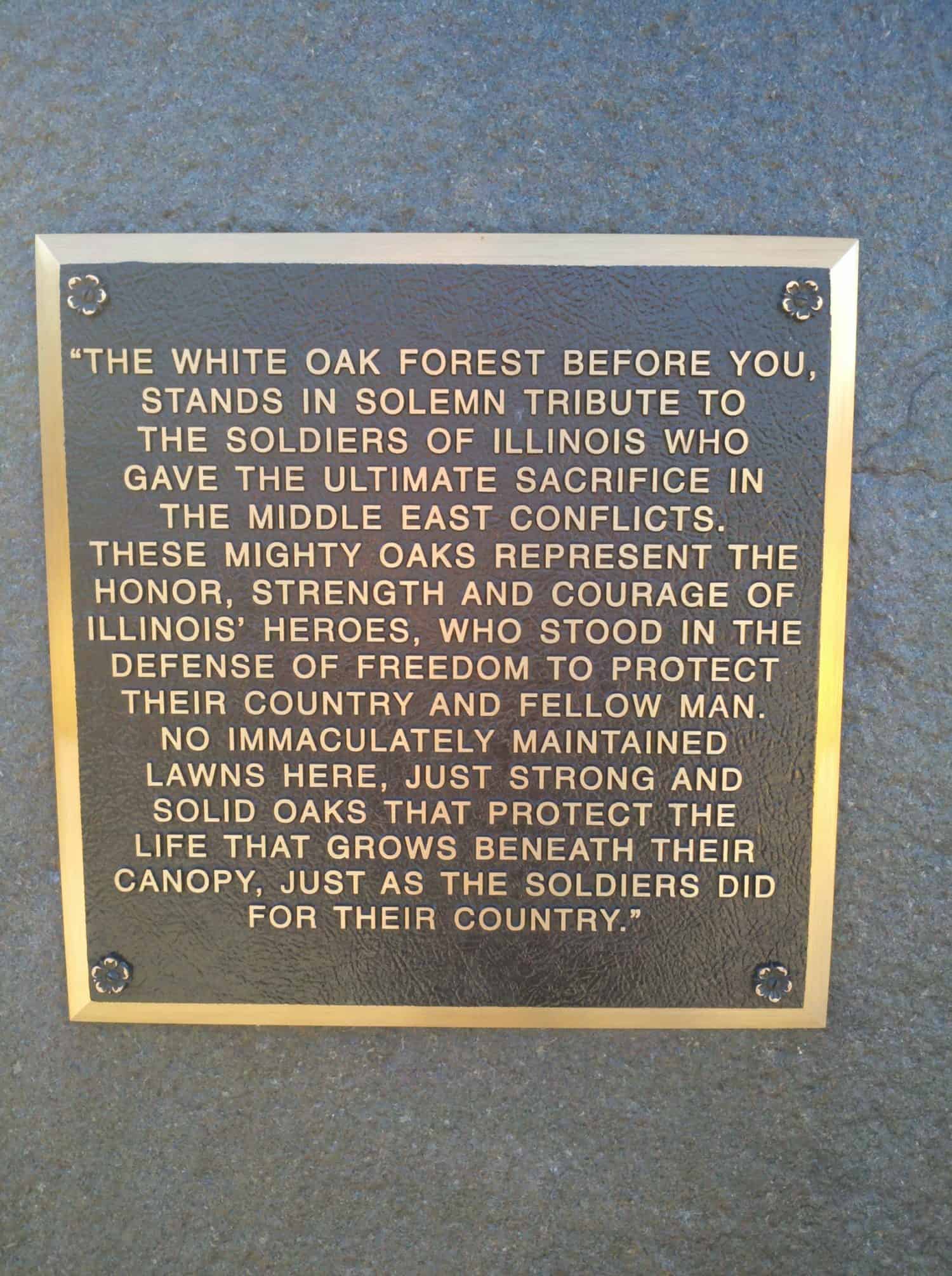 Bronze plaque honors Illinois soldiers who died in Middle East conflicts, comparing their sacrifice to the strength and protection of oak trees, with engraved text on a stone background.